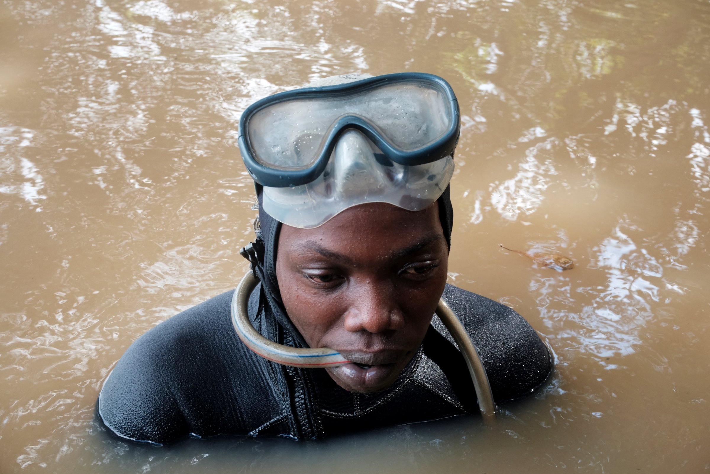 Oscar plonge pour guider l'aspirateur de la drague, sur le fleuve Cavally, au Liberia (juin 2025).
