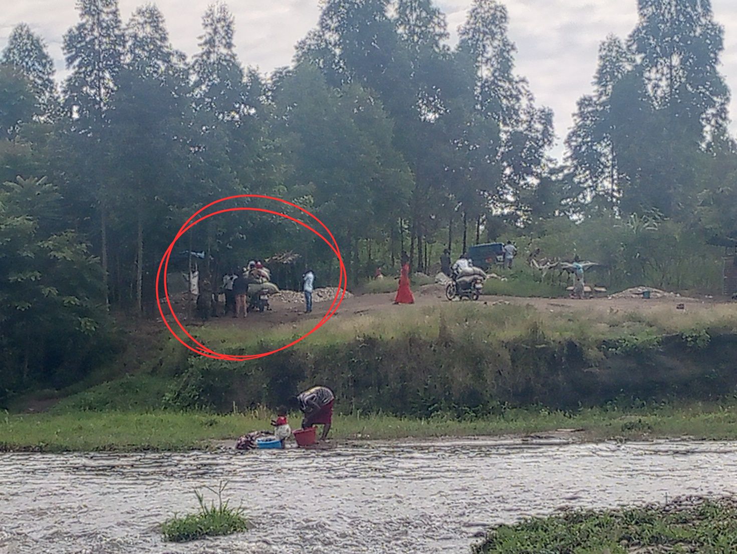En arrière-plan de cette image capturée clandestinement par Ukweli sur la piste de Kamuchanga, à Kasindi-Lubiriha, des militaires ougandais perçoivent de l'argent auprès d'un trafiquant (à bord d'une moto) alors que d'autres trafiquants attendent leurs clients à côté d'une position militaire (à droite).