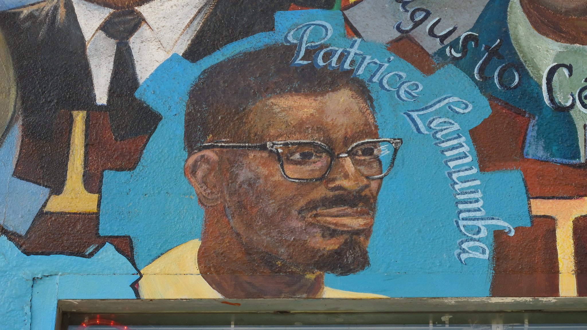 The image features a mural that includes a portrait of a man with glasses and a beard, identified as Patrice Lumumba. He is depicted in a colorful artistic style, wearing a yellow shirt. The mural may also include other figures or elements, but this particular part focuses on Lumumba's likeness alongside his name, highlighting his significance. The background is vibrant, contributing to the overall visual impact of the mural.