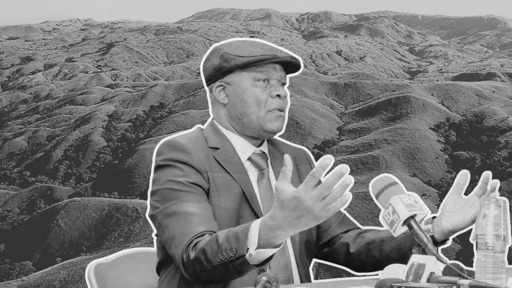 The image features a man in a suit and a cap, gesturing while speaking at a press conference or similar setting. He appears to be in front of a landscape of rolling hills or mountains, which are shown in a monochrome style to highlight the subject. The background scenery emphasizes the natural environment, contrasting with the formal attire of the man, who seems to be making an important point. The overall composition combines elements of nature and a formal discussion.
