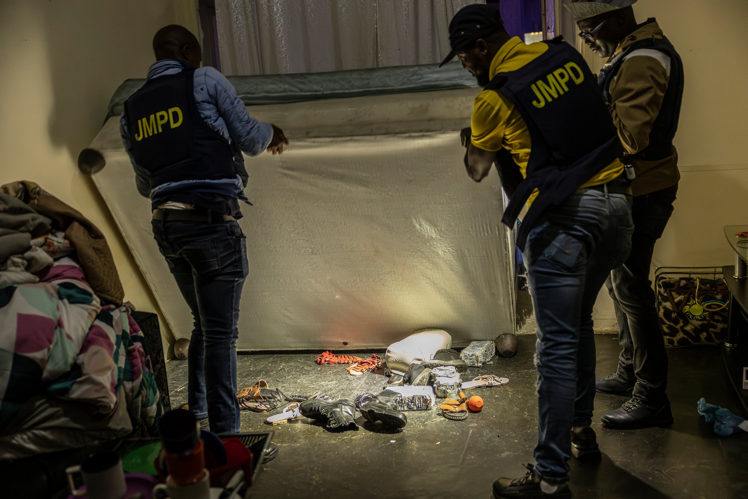 Des agents du Département de police métropolitain de Johannesburg (JMPD) inspectent sous le lit d'un résident (18 décembre 2025).