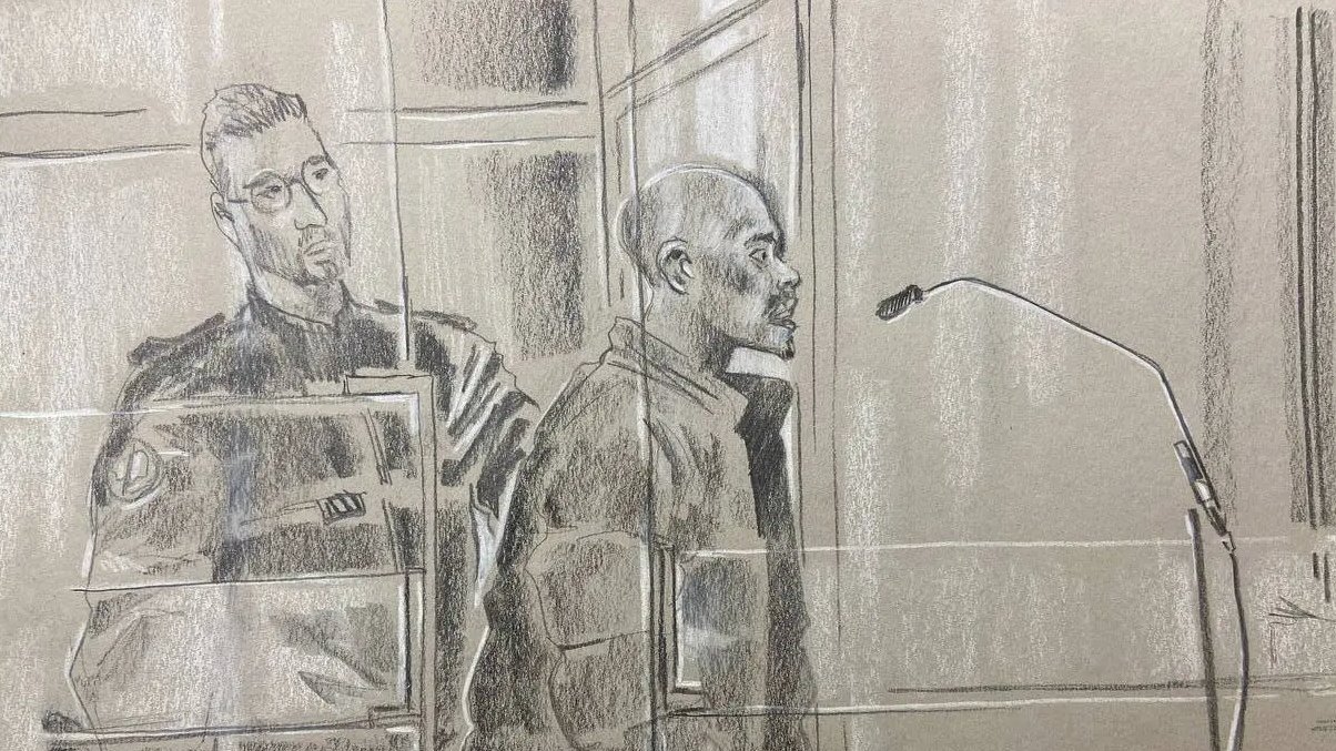 L'image représente une scène d'audience judiciaire. Au premier plan, on voit un homme debout, probablement un accusé, qui se tient derrière un panneau de séparation, exprimant une attitude sérieuse. Il est entouré par des éléments du tribunal, comme un microphone devant lui, indiquant qu'il pourrait s'exprimer. À sa gauche se trouve un policier en uniforme, affichant une posture attentive et vigilant. L'atmosphère de l'image est solennelle, reflétant le sérieux de la situation judiciaire. Les couleurs utilisées sont principalement des nuances de gris, et le style est esquissé, avec un rendu qui transmet les émotions et la tension de l'instant.