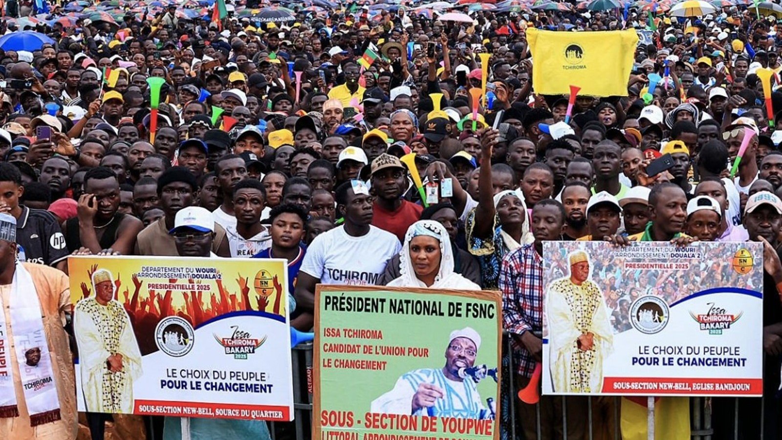 L'image montre une grande foule rassemblée pour un événement ou un meeting public. Les gens se tiennent serrés les uns contre les autres, créant une mer de visages et de vêtements colorés. De nombreux participants tiennent des banderoles avec des messages politiques, notamment le slogan "Le choix du peuple pour le changement." On peut également apercevoir des drapeaux flottants, évoquant une atmosphère de mobilisation et d'engagement. L'arrière-plan suggère une ambiance urbaine, avec des bâtiments visibles au loin, tandis que le ciel pourrait être nuageux ou couvert. Ce rassemblement dégage un sentiment d'énergie collective, d'espoir et de désir de changement.