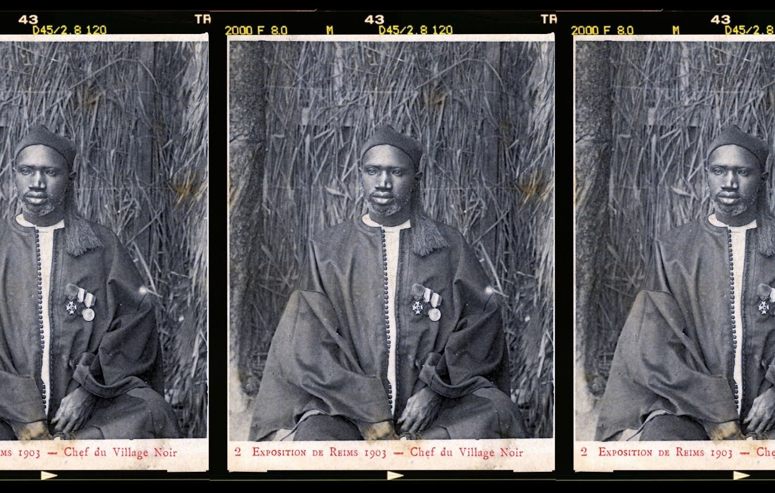L'image présente trois portraits en noir et blanc d'un homme en costume traditionnel. Il est assis sur un fond de paille tressée qui évoque un environnement naturel. L'homme porte une tenue ample, probablement en textile sombre, et est décoré de plusieurs médailles accrochées à sa poitrine, ce qui suggère un statut élevé ou une reconnaissance. Son visage présente une expression solennelle et sérieuse. Les portraits sont disposés côte à côte, créant une composition symétrique. Cette image témoigne d'un moment historique, probablement lié à une exposition ou un événement marquant.