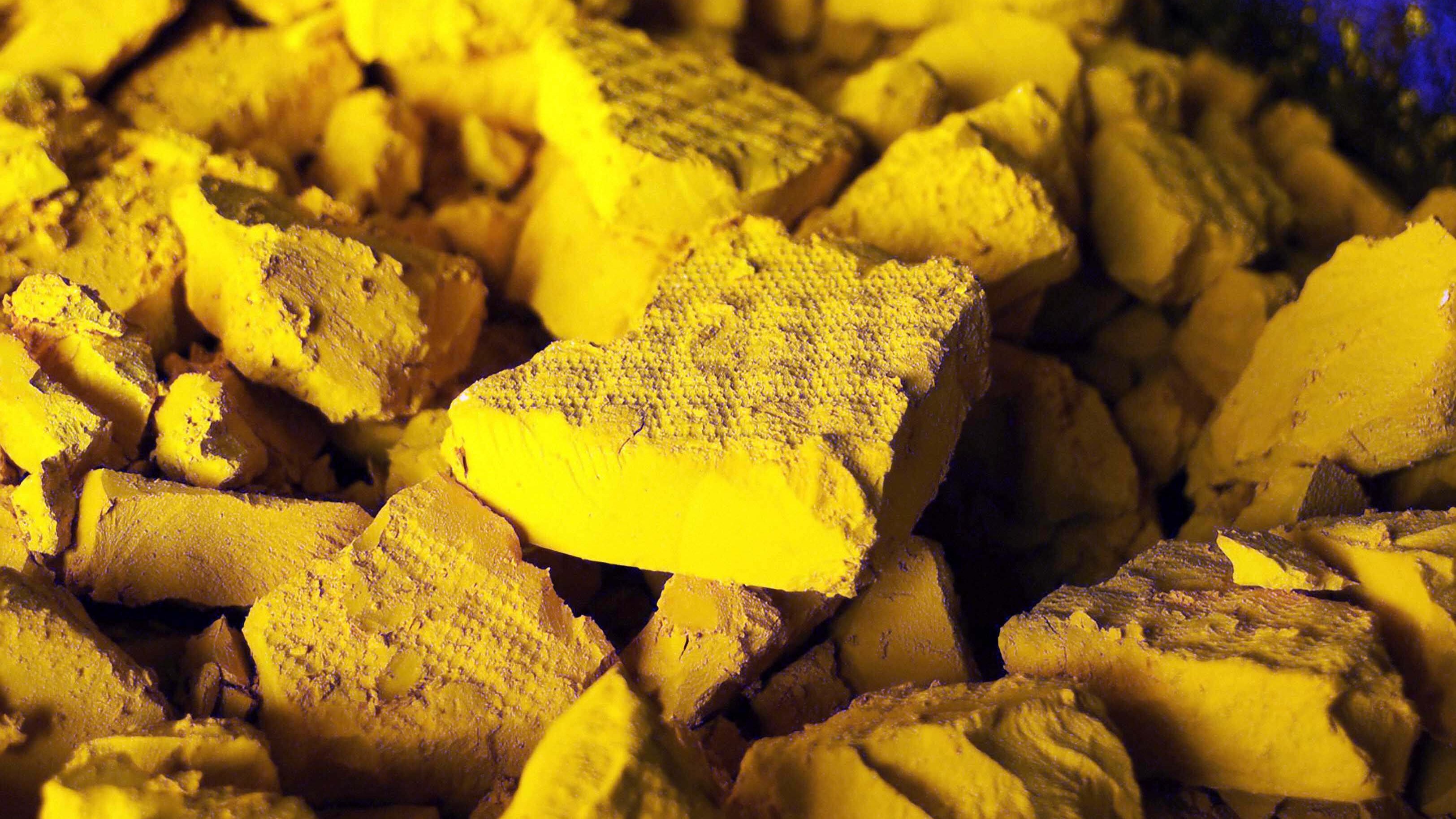 L'image montre un tas de morceaux de matière d'une couleur jaune vif. Les morceaux sont anguleux et irréguliers, présentant des surfaces rugueuses et poudreuses. La lumière semble créer des ombres subtiles, accentuant les textures des éclats. L'ensemble de la composition transmet une impression de dépouillement et de matière brute, évoquant à la fois la richesse de la couleur et une certaine fragilité des formes.