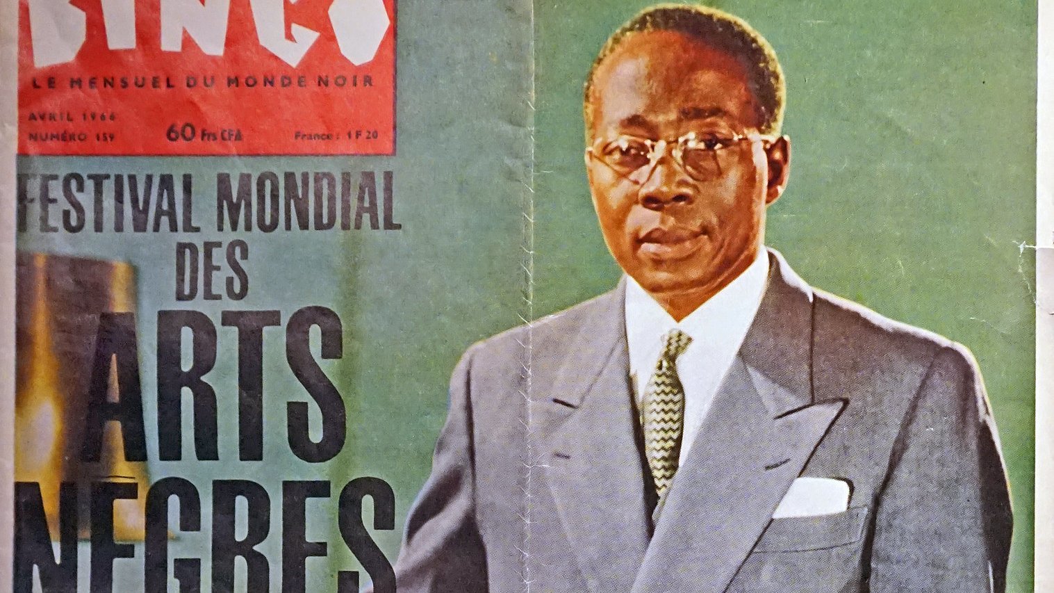 L'image représente une couverture de magazine intitulée "Bingo", datée d'avril 1966. Au premier plan, un homme debout est habillé d'un costume clair, avec une chemise blanche et une cravate sombre. Il porte des lunettes et affiche une expression sérieuse. L'arrière-plan est flou, mais semble être un environnement sobre, mettant en valeur le sujet. En haut de la couverture, on peut lire "FESTIVAL MONDIAL DES ARTS NÈGRES", ce qui évoque un événement culturel important. Les couleurs du magazine sont douces, ajoutant une touche d'élégance à l'ensemble.