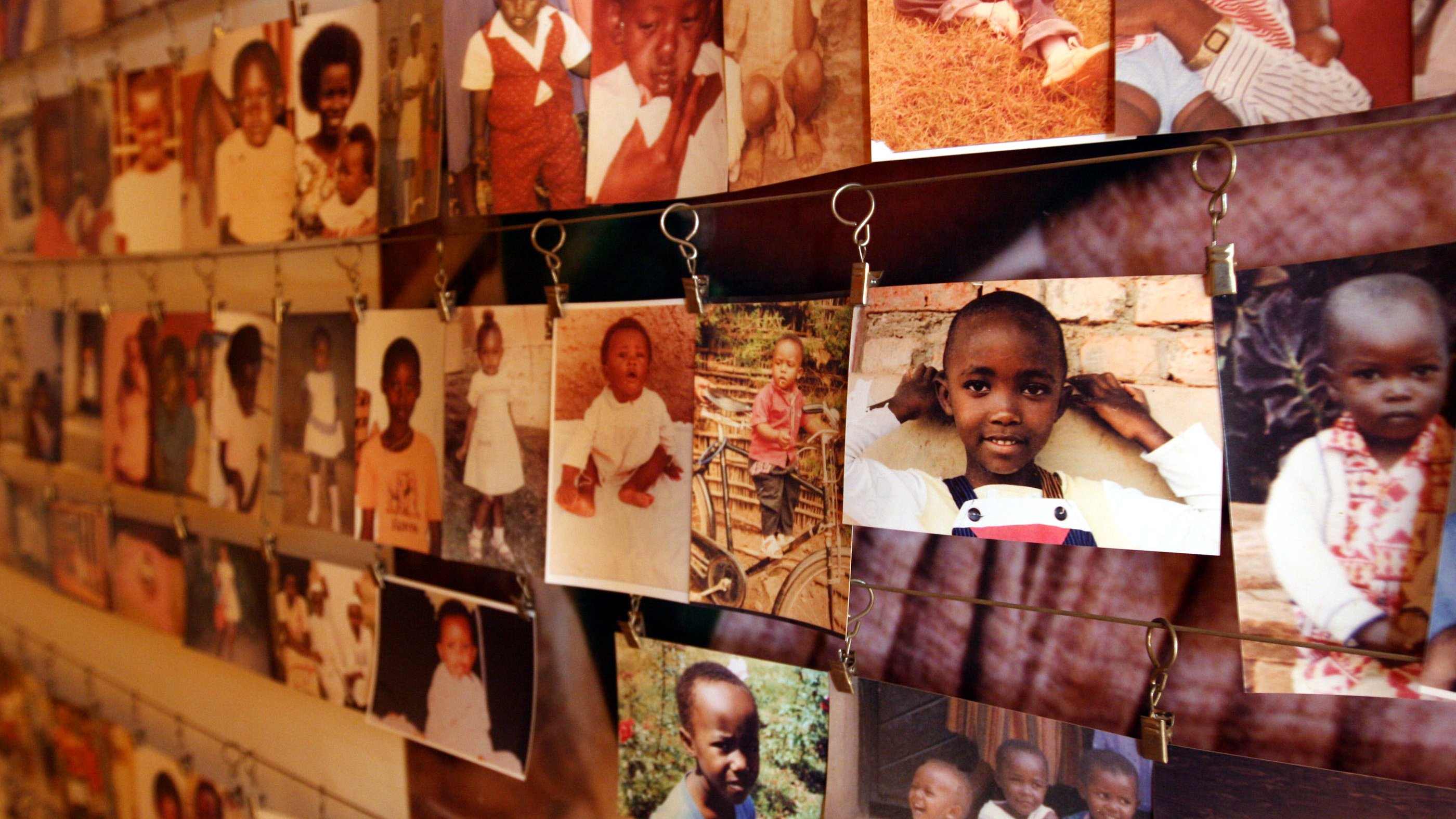 L'image montre un grand mur couvert de nombreuses photos accrochées avec des pinces. Ces images, en couleur et en noir et blanc, illustrent des enfants de différents âges, principalement des jeunes enfants. Les visages des enfants expriment souvent des sourires ou des poses amusantes. Les photos sont en désordre, ce qui crée une scène vivante et nostalgique, évoquant des souvenirs d'enfance. Le fond est neutre, permettant aux photos de se démarquer et de raconter des histoires individuelles de joie et d'innocence.