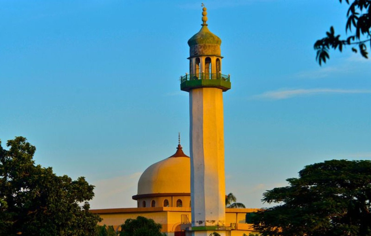 L'image montre un groupe de personnes en train de prier ensemble. Au centre, un homme en costume bleu se tient les mains jointes, la tête légèrement inclinée, montrant une attitude de recueillement. Autour de lui, plusieurs hommes portent des vêtements traditionnels, incluant des turbans et des chapeaux décorés. Tous semblent concentrés et tournés vers l'avant, les yeux fermés ou la tête baissée, dans un moment de méditation ou de prière. L'ambiance est empreinte de sérénité et de respect.