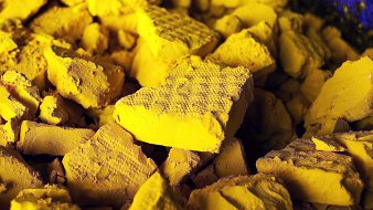 L'image montre un tas de morceaux de matière d'une couleur jaune vif. Les morceaux sont anguleux et irréguliers, présentant des surfaces rugueuses et poudreuses. La lumière semble créer des ombres subtiles, accentuant les textures des éclats. L'ensemble de la composition transmet une impression de dépouillement et de matière brute, évoquant à la fois la richesse de la couleur et une certaine fragilité des formes.