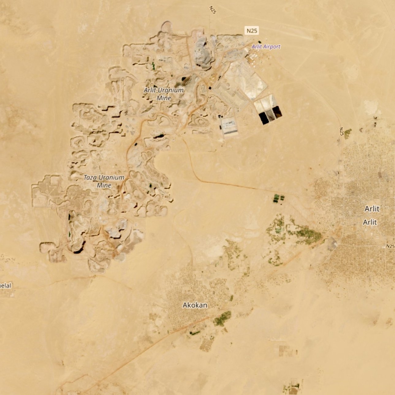 The image appears to be an aerial view of a desert landscape featuring two distinct areas. On the left side, there are ruins or archaeological sites, indicated by clusters of structures, possibly remnants of ancient buildings. Nearby, there is an airport and some roads connecting the areas. On the right side, there is a more densely populated area, showing what looks like a town or settlement named "Antic," characterized by a grid-like pattern, suggesting regular streets and organized layout. Surrounding the settlement, there are patches of greenery, likely indicating agricultural activity. The vast surrounding landscape is primarily sandy and barren, typical of desert regions.