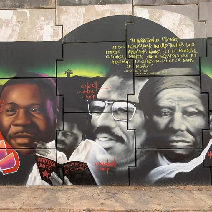 Cette image montre une fresque murale vibrante et colorée qui rend hommage à des figures importantes de l'histoire africaine. Au centre, il y a des portraits de trois personnes, chacun portant une expression sérieuse et réfléchie. Les visages sont peints en noir et blanc, mettant en valeur les détails de leurs traits. À gauche, un homme sourit légèrement, symbolisant l'espoir et la détermination. Au centre, un homme barbu porte des lunettes et affiche un regard intense, représentant la sagesse. À droite, un homme au visage marqué par le temps semble contemplatif, illustrant la profondeur de la pensée. En arrière-plan, des motifs géométriques et des couleurs riches ajoutent une dynamique à l'ensemble. Des inscriptions en lettres blanches ponctuent la fresque, partageant des pensées inspirantes sur l'identité, la culture et l'impact de ces figures dans le monde. Cette œuvre évoque une ambiance de fierté et d'émancipation culturelle.