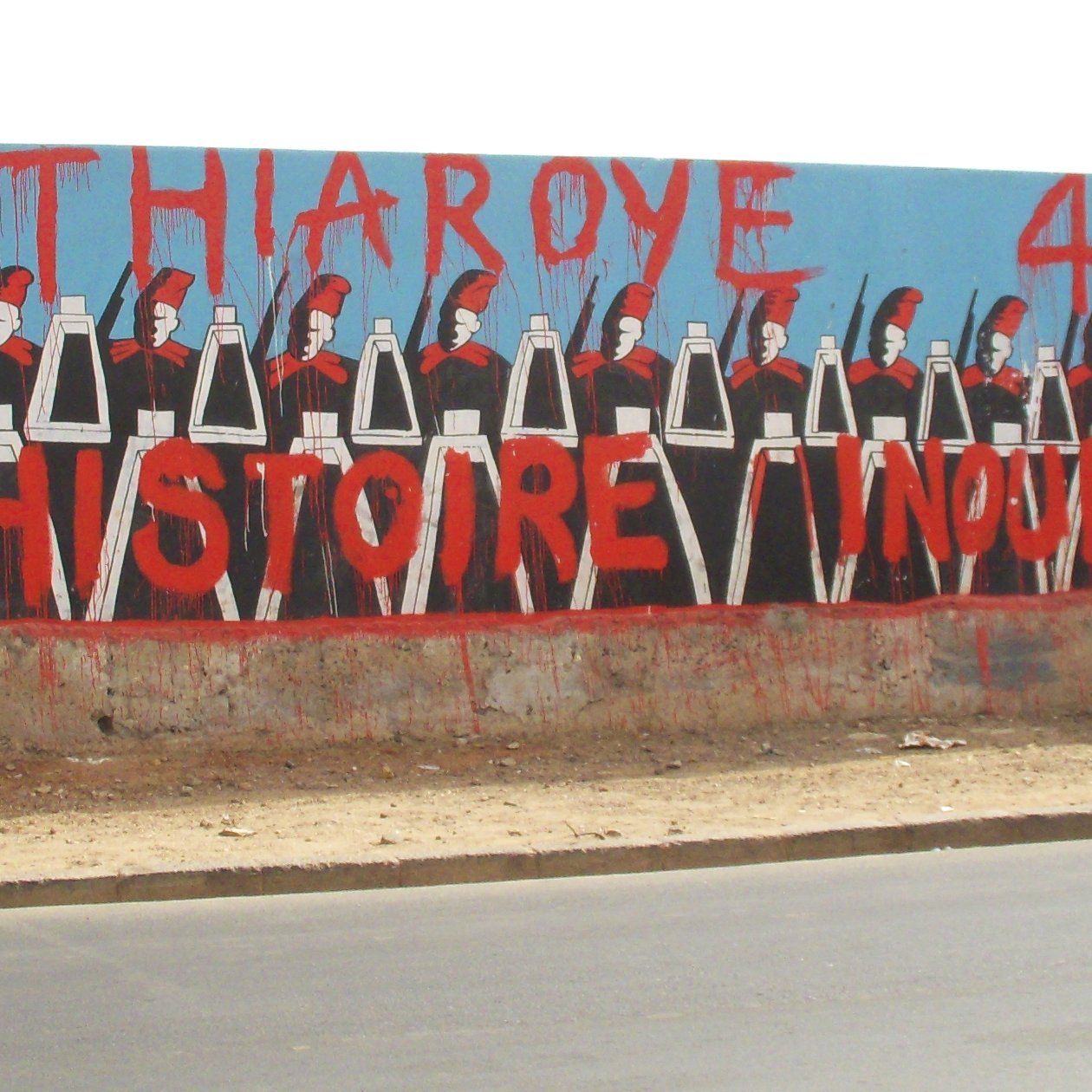 L'image montre une grande fresque murale peinte sur un mur. Au premier plan, on voit une rangée de silhouettes représentant des soldats, chacun portant un uniforme noir et un casque. Ils sont alignés de manière uniforme, les bras le long du corps. En arrière-plan, le mur est peint en bleu, ce qui fait ressortir les personnages. En haut, on peut lire en grandes lettres rouges le texte "THIAROYE 44", et en dessous, "UNE HISTOIRE INOUBLIABLE". Cette œuvre évoque une mémoire historique importante, probablement liée à des événements marquants qui ont eu lieu à Thiaroye, une ville du Sénégal. L'ensemble de l'image crée une ambiance à la fois sérieuse et respectueuse, honorant un passé collectif.