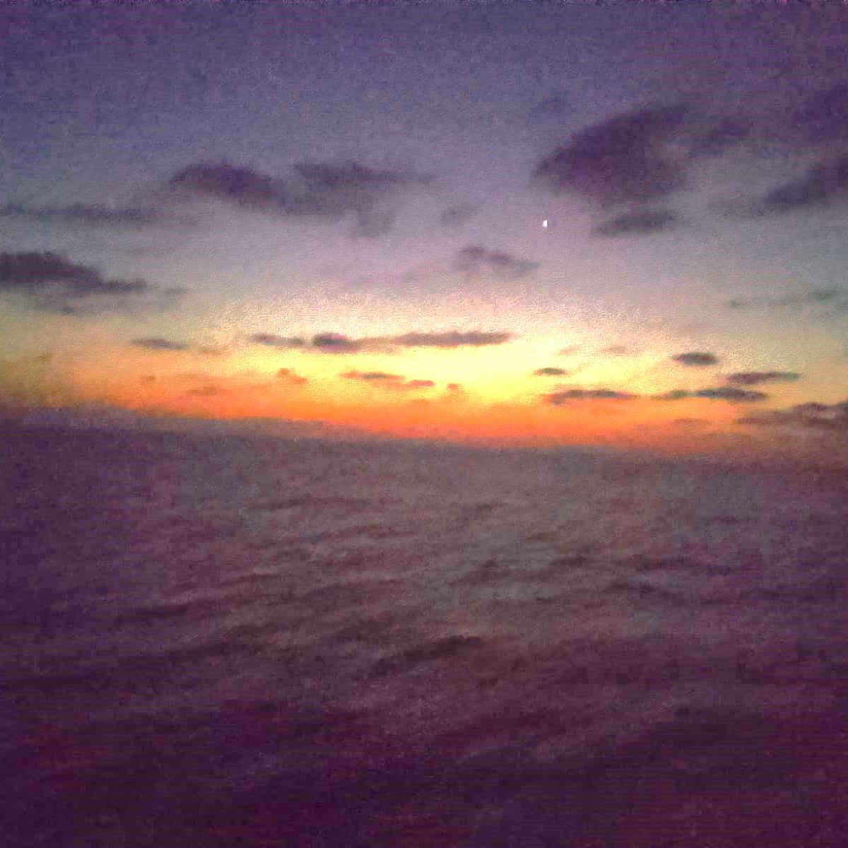 Cette image montre un paysage maritime au crépuscule. Le ciel est teinté de nuances sombres, avec des nuages épars. On remarque un doux dégradé de couleurs allant du bleu foncé au orange, signalant la transition entre le jour et la nuit. L'horizon est légèrement flou, et l'eau semble calme, reflétant les couleurs du ciel. Une étoile brillante est visible dans la partie supérieure de l'image, ajoutant une touche de mystère à cette scène sereine et nocturne. L'atmosphère générale est paisible et contemplative.
