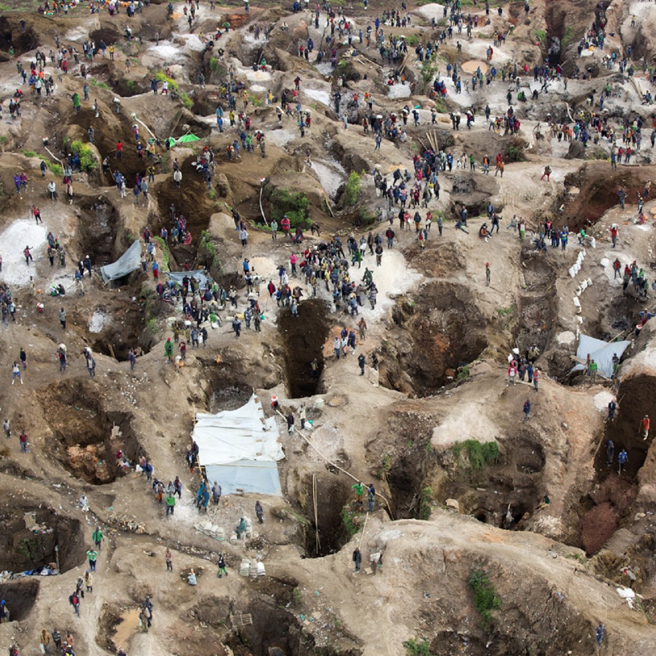 L'image représente une grande site d'extraction minière, probablement un lieu de prospection. On y voit de nombreuses personnes, qui semblent être des mineurs ou des chercheurs de minerai, dispersées sur un terrain accidenté. Le sol est parsemé de nombreuses cavités, témoignant des efforts de creusement. Certaines zones sont abritées par des abris temporaires en toile, tandis que d'autres sont à ciel ouvert. La scène dégage une dynamique de travail acharné, où les individus s'affairent dans un environnement à la fois désordonné et organisé, caractérisé par des monticules de terre et des roches. L'ensemble évoque un lieu de quête et de lutte pour des ressources précieuses.