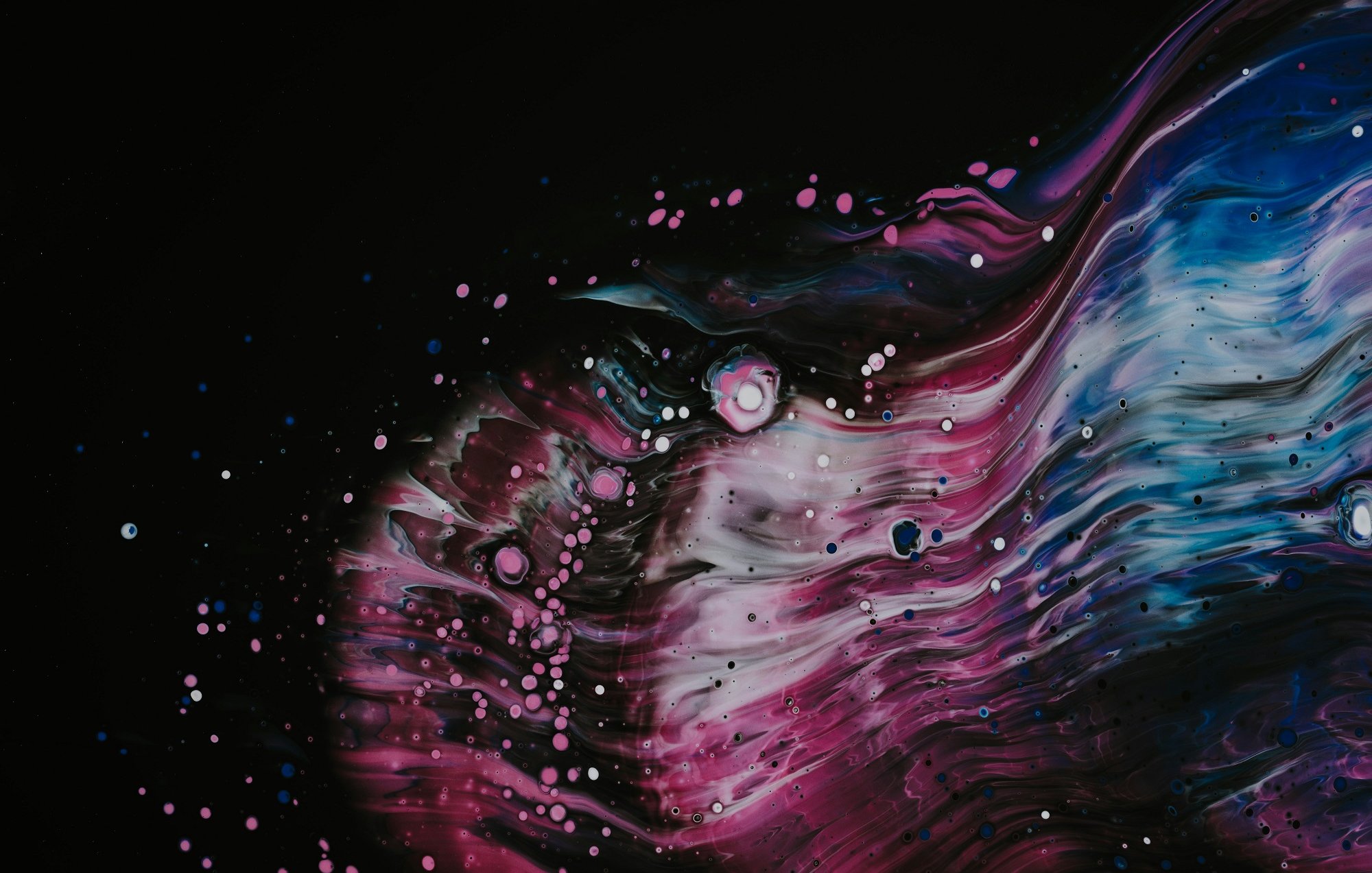 L'image présente une explosion de couleurs vibrantes sur un fond noir, évoquant un cosmos mystérieux. Des ondulations fluides rappellent des vagues, avec des nuances de bleu, de rose et de violet se mêlant harmonieusement. Des éclats de blanc, semblables à des étoiles dispersées, ajoutent une dimension de profondeur et de texture, créant une atmosphère dynamique et captivante. L'ensemble évoque un mouvement constant, presque euphorique, incitant à l'évasion et à la contemplation.