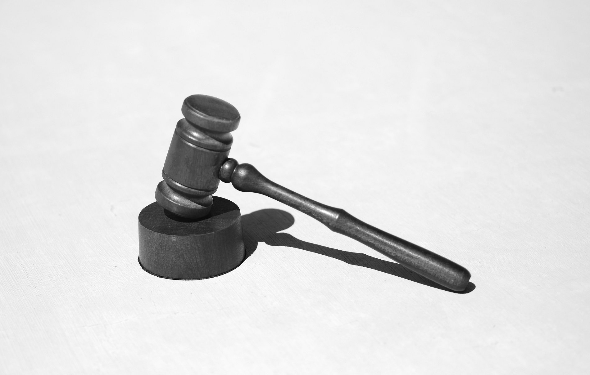 L'image présente un maillet de juge, souvent appelé "gavel". Il est en métal noir, avec une partie cylindrique plus épaisse à sa base et un long manche. Le maillet repose sur une surface claire, ce qui crée un contraste marqué. La lumière éclaire l'objet, projetant une ombre sur le côté. Le maillet est couramment associé au monde de la justice et des tribunaux, symbolisant l'autorité et la prise de décision.