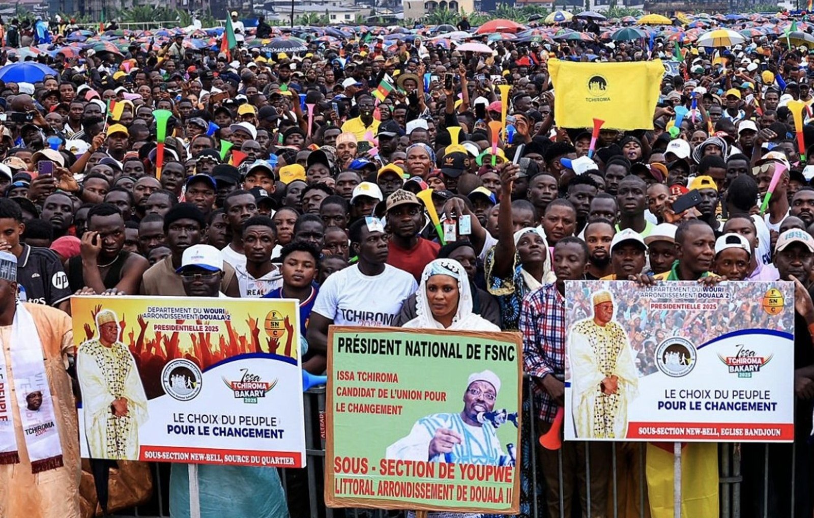 L'image montre une grande foule rassemblée pour un événement ou un meeting public. Les gens se tiennent serrés les uns contre les autres, créant une mer de visages et de vêtements colorés. De nombreux participants tiennent des banderoles avec des messages politiques, notamment le slogan "Le choix du peuple pour le changement." On peut également apercevoir des drapeaux flottants, évoquant une atmosphère de mobilisation et d'engagement. L'arrière-plan suggère une ambiance urbaine, avec des bâtiments visibles au loin, tandis que le ciel pourrait être nuageux ou couvert. Ce rassemblement dégage un sentiment d'énergie collective, d'espoir et de désir de changement.