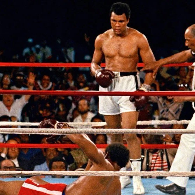 L'image montre un moment mémorable d'un match de boxe. Au centre, un boxeur, torse nu et portant des shorts blancs, se tient debout avec un regard déterminé. C'est Muhammad Ali, connu pour sa rapidité et sa technique. À ses pieds, un autre boxeur est allongé sur le sol, faisant face au ring, après avoir été mis au tapis. Le public en arrière-plan est en émoi, certains levant les bras en signe d'enthousiasme ou d'étonnement. Un arbitre, vêtu d'un maillot à rayures, s'approche du boxeur au sol, prêt à commencer le compte. L'atmosphère est chargée d'intensité et d'adrénaline, typique des combats de boxe.
