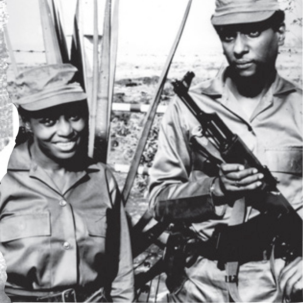 Dans cette image en noir et blanc, nous voyons un couple assis à une table dans un restaurant. La femme, à gauche, porte une coiffure textile colorée et des boucles d'oreilles larges. Elle semble concentrée sur son assiette, peut-être en train de couper ou de préparer de la nourriture. À sa droite, un homme tient un bébé dans ses bras, regardant la femme avec bienveillance. Le bébé est emmitouflé dans une couverture. En arrière-plan, d'autres personnes sont visibles, créant une atmosphère animée de rassemblement convivial. Les tables sont dressées avec des couverts et des verres, ajoutant une touche d'élégance à la scène.