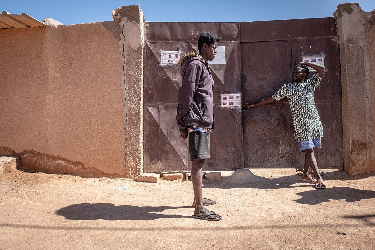 L'Ivoirien Khalifa (à droite) discute devant la porte du ghetto qu'il gère pour le compte d'un passeur sénégalais, dans le quartier de Doubai à Agadez.