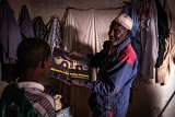 Inside his home in Akokan, Boukari Mahaman, a former Cominak worker, shows one of his sons a photo of a large mining machine similar to those he used when he worked in the uranium mines.