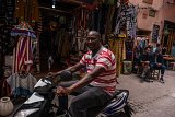 Racine Ba traverse en scooter les ruelles étroites du souk de Marrakech pour se rendre dans le riad où il travaille.