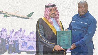 The image depicts a formal ceremony where two men are exchanging a green plaque or certificate. One man is dressed in traditional Saudi attire, including a thobe and a headscarf, while the other is wearing a blue suit. In the background, there is an airplane flying and a group of people holding a banner, possibly in connection to a pilgrimage or religious gathering. The overall tone suggests a celebration or accomplishment related to travel or cooperation, likely involving Saudi Arabia.
