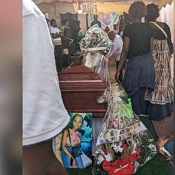 L'image montre un moment poignant d'un enterrement. Au centre, un cercueil en bois brun, sur lequel sont déposés des bouquets de fleurs. À côté du cercueil, une grande photo d'une femme est accrochée, entourée de décorations florales et de bandes de tissu. Des personnes, visiblement en deuil, se rassemblent autour, certaines portant des vêtements sombres. L'ambiance est sombre mais respectueuse, marquée par la tristesse et l'hommage à la personne décédée. L'arrière-plan est flou, mais on peut deviner une tente qui abrite cette cérémonie. L'ensemble évoque des sentiments de perte et de commémoration.